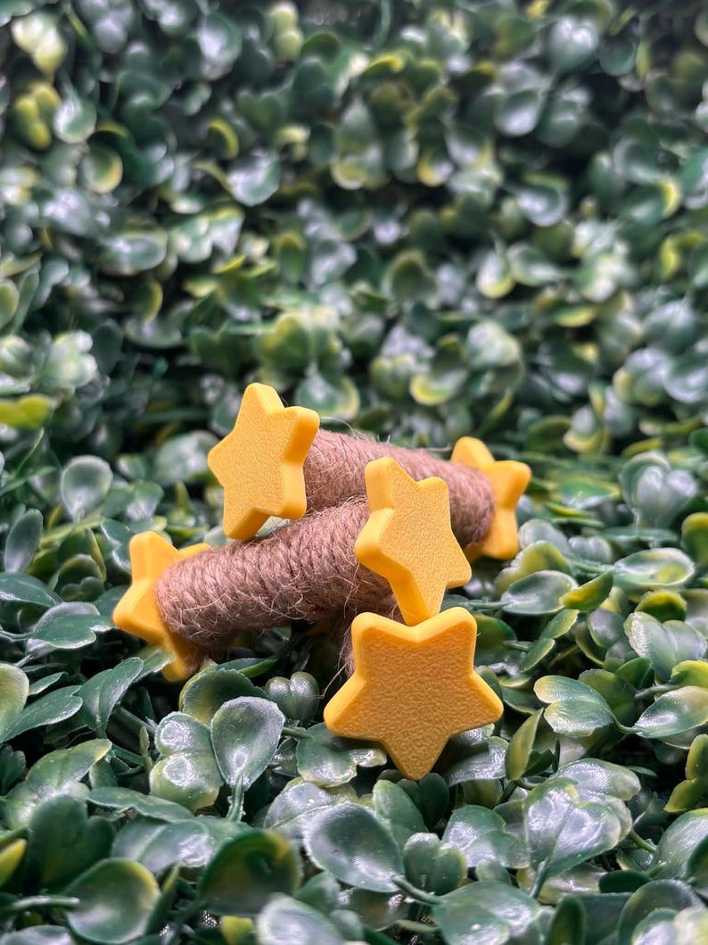 May include: A close-up of yellow star-shaped embellishments on a brown twine bundle, set against a backdrop of green foliage. The stars are evenly spaced and appear to be made of a solid material. The twine is tightly wound.
