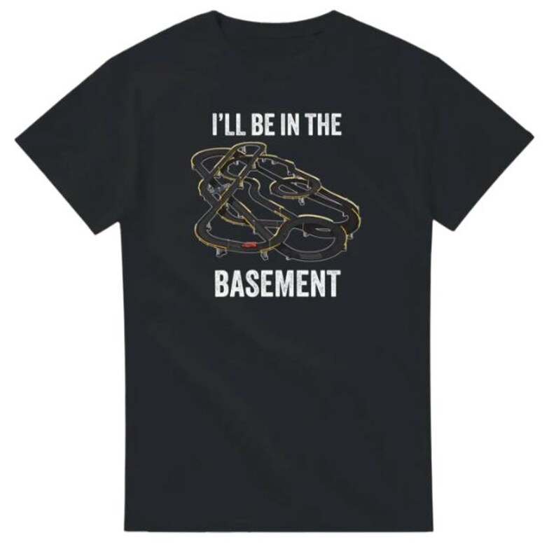 May include: Black t-shirt with the text "I'll Be In The Basement" above a graphic of a race track. The track design is in shades of gray and gold.