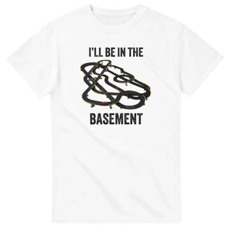 May include: White t-shirt with the text "I'll Be In The Basement" in black font. The shirt features a graphic of a black and gold slot car track. A fun and playful design for hobbyists.