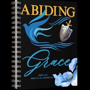 Può includere: Un quaderno a spirale nero con le parole "ABIDING Grace" in oro e blu. Il design della copertina include una colomba blu, uno scudo e una spada e un elemento floreale. I versetti biblici sono stampati in basso.