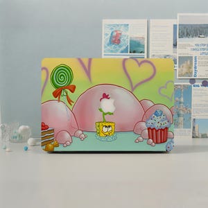 May include: A laptop skin featuring a yellow sponge character with a square body, a green lollipop with a red bow, a cupcake with blue frosting, and a slice of cake. The background is light green with pink bubble shapes and purple heart outlines.