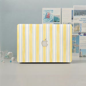 May include: A laptop computer featuring a protective cover with a vertical striped pattern in shades of yellow and light blue. The cover has a smooth finish and displays the silver Apple logo centered on the back of the closed device.