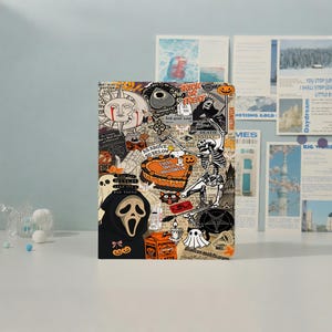 May include: A rectangular notebook featuring a collage of Halloween-themed illustrations including a skeleton, a ghost, a masked figure, a pumpkin, and text such as "Trick or Treat," "As Above So Below," and "You Say Witch Like It's A Bad Thing."