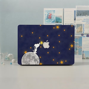 May include: A dark blue laptop skin featuring a graphic of Snoopy standing on a grey moon, reaching for a yellow star. The design includes scattered yellow stars across a deep blue background and incorporates the silver Apple logo cutout.