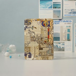 Può includere: Una custodia rettangolare per tablet con una stampa dettagliata in stile manoscritto medievale. Il design include calligrafia complessa e illustrazioni di un drago, un cavaliere, un unicorno e una spada in tonalità oro, blu e marrone.