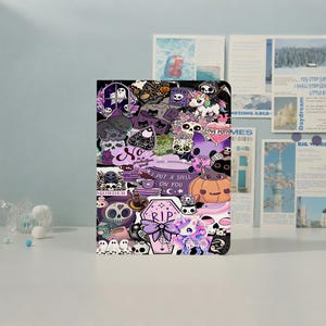 Pode incluir: Um caderno retangular com uma colagem de autocolantes roxos, pretos e brancos. O design inclui fantasmas, crânios, uma abóbora, unicórnios e o texto que diz "No is a protection spell", "I put a spell on you" e "R.I.P."