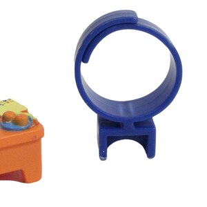 May include: A collection of miniature toys, including a blue ring, a small desk with art supplies, and a doll figure wearing overalls. The desk is orange with a blue back, and the doll has yellow hair.