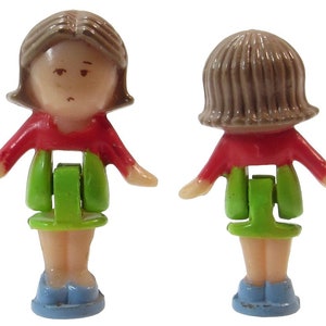 May include: A small plastic doll with brown hair, a red shirt, a green skirt, and blue shoes. The doll is articulated at the waist and can be posed in different positions.