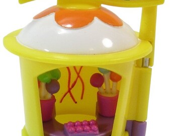 May include: A yellow Polly Pocket playset shaped like a carousel with a pink heart on the bottom. The carousel has a purple counter with a row of pink and purple candies. The top of the carousel has a white roof with an orange trim and a yellow banner with a cartoon image of a carousel with two horses and stars.