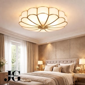 May include: A decorative ceiling light fixture with a floral design. The light has a gold-colored frame and a white, petal-shaped shade. The fixture is mounted on a white ceiling in a bedroom setting.
