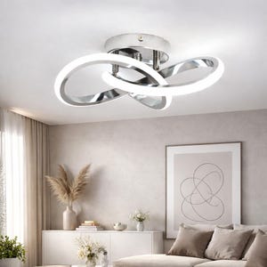 May include: Modern chrome ceiling light fixture with three interconnected, curved, illuminated rings. The light has a polished metal finish and emits a bright, white light. The fixture is mounted on a white ceiling in a living room setting.
