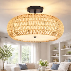 May include: A woven rattan flush mount ceiling light fixture. The light has a black base and a natural beige woven shade. The light is oval-shaped and provides soft, ambient lighting. The fixture is suitable for a living room or bedroom.