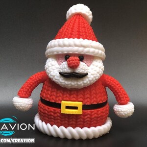 May include: A knitted Santa Claus figurine with a red hat and suit, white beard, and black mustache. The figure has a black belt with a yellow buckle. The base and hat trim are white. The image includes the text "CREAVION" and "PATREON.COM/CREAVION".