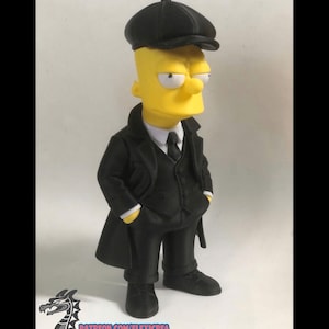 May include: A yellow cartoon character figurine wearing a black flat cap, a black overcoat, a black vest, a white collared shirt, and a black tie. The character has a serious expression and hands in pockets. A dragon logo and text are visible at the bottom.