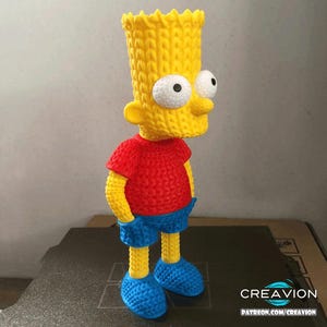 May include: A 3D-printed Bart Simpson figurine. It has a yellow knitted-style head and body, a red shirt, blue shorts, and blue shoes. The figurine has large white eyes. It is standing on a dark surface.