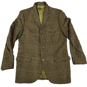 May include: A tweed blazer in a brown and olive green plaid pattern. The jacket has a notched lapel, three buttons, and two front pockets. The interior lining is a light green color.
