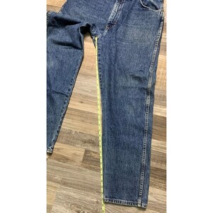May include: Blue denim jeans with a straight leg cut. A yellow measuring tape is placed along the length of the jeans. The jeans have a classic five-pocket design and a button and zipper closure.