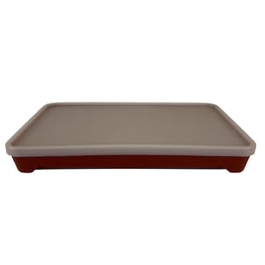 Puede incluir: Un recipiente rectangular para almacenar alimentos con una base roja y una tapa gris claro. La tapa tiene un borde ligeramente elevado y encaja perfectamente en la base. El recipiente está diseñado para almacenar alimentos.