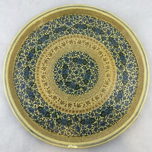 May include: Round decorative tray with a floral design. The tray features a cream-colored border and a central pattern of blue flowers on a dark background. The inner circle has a brown and gold leaf pattern.