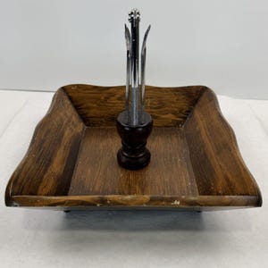 May include: A vintage wooden serving tray with a dark brown finish. The tray has a square shape with wavy edges. A dark brown wooden holder in the centre holds several stainless steel nut picks and a nutcracker.