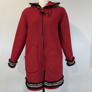 May include: A red hooded coat with a black zipper, two front pockets, and decorative trim on the cuffs and hem. The trim features black, white, and red accents. The coat is displayed on a mannequin.