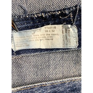 May include: Close-up of blue denim jeans with a tag. The tag displays the size 50 x 32 and washing instructions. The jeans have a classic five-pocket design and a button and zipper closure.