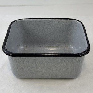 May include: A rectangular, enamelware container with a speckled gray interior and a black rim. The sides are straight, and the corners are rounded. The container is empty and sits on a white surface.