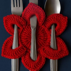 Peut inclure: Gros plan d'un ensemble de couverts, comprenant une fourchette, un couteau et une cuillère, sur un fond bleu foncé. Les ustensiles sont partiellement recouverts d'un dessous de plat en forme de fleur rouge vif, crocheté.