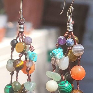 Peut inclure: Boucles d'oreilles artisanales composées d'une cascade de pierres précieuses colorées. Les boucles d'oreilles ont des crochets en argent et sont montées sur un cordon marron. Les pierres comprennent la turquoise, l'œil de tigre, la malachite et l'agate.