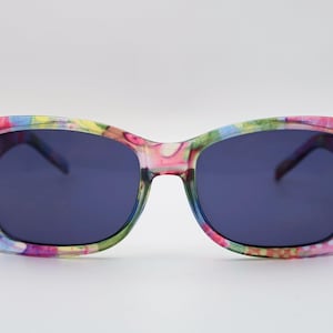 May include: Sunglasses with a colorful floral pattern on the frames. The lenses are a dark blue color. The frames have a mix of pink, yellow, green, and blue hues.