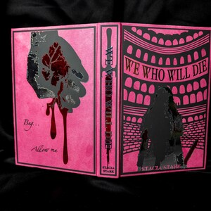 May include: A pink book cover with the title "WE WHO WILL DIE" in black text. The cover features a hand silhouette with a red leaf design and dripping blood. The spine reads "WE WHO WILL DIE" vertically.