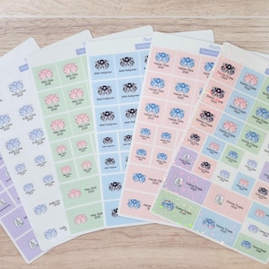 May include: Five rectangular sticker sheets featuring grids of small square labels in pastel shades of purple, green, blue, and pink. Each individual sticker contains a small graphic icon and printed text, including names and years like 2020.