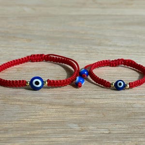 May include: Two red woven bracelets with blue and white evil eye beads. The bracelets have a sliding knot closure for adjustable sizing. The evil eye beads are blue with a white center and gold accents.