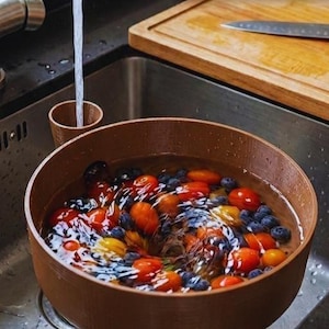Op de afbeelding: Een roestvrijstalen keukenkraan met water dat in een bruine kom stroomt, gevuld met kleurrijk fruit en groenten. De tekst op de afbeelding luidt "TORNADO-EFFECT FRUIT & VEGETABLE WASHER."