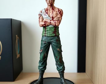 Peut inclure: Figurine détaillée d'un personnage de la série animée One Piece. La figurine a les cheveux verts, un sous-vêtement blanc et un pantalon vert. La figurine est couverte de peinture rouge et se tient sur une base noire et dorée avec le logo One Piece.