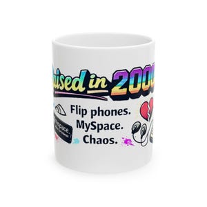 May include: White ceramic mug with the text "Raised in 2000s" in a colorful, retro font. The mug features graphics of a flip phone, MySpace logo, headphones, and a broken heart. The mug is a nostalgic item.