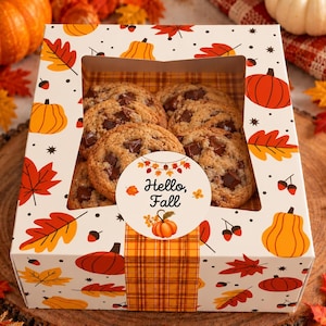 May include: A square white cardboard box filled with chocolate chip cookies, featuring a window and a pattern of orange pumpkins, red and yellow autumn leaves, and acorns. A round sticker on the front reads Hello, Fall with a pumpkin graphic.