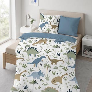 Può includere: Un set di copripiumino e cuscini bianchi con un motivo a dinosauri. Il design presenta vari dinosauri in tonalità di blu, verde e marrone, insieme a palme e fogliame. Il set include un cuscino blu e una federa abbinata.