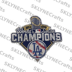 Könnte beinhalten: Gestickter Aufnäher mit dem Text "World Series Champions" und den Jahreszahlen "2020" und "2020". Er zeigt das Logo der Los Angeles Dodgers und Baseball-Details in Blau, Weiß und Gold. Für Sportfans.