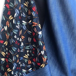 Puede incluir: Primer plano de una tela con un estampado de lib&eacute;lulas en rojo, amarillo, azul y blanco sobre un fondo azul marino. La tela estampada se combina con un material azul liso similar al denim, creando un contraste de texturas y colores.