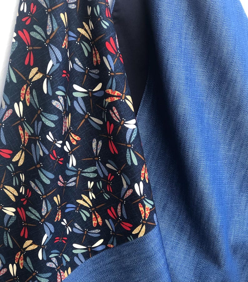 Puede incluir: Primer plano de una tela con un estampado de lib&eacute;lulas en rojo, amarillo, azul y blanco sobre un fondo azul marino. La tela estampada se combina con un material azul liso similar al denim, creando un contraste de texturas y colores.