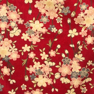 May include: Red fabric with a white and pink floral pattern. The flowers are stylized cherry blossoms.