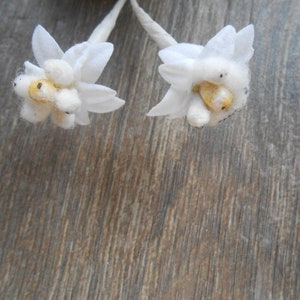 May include: Two white fabric flowers with yellow centres on a brown wooden background.