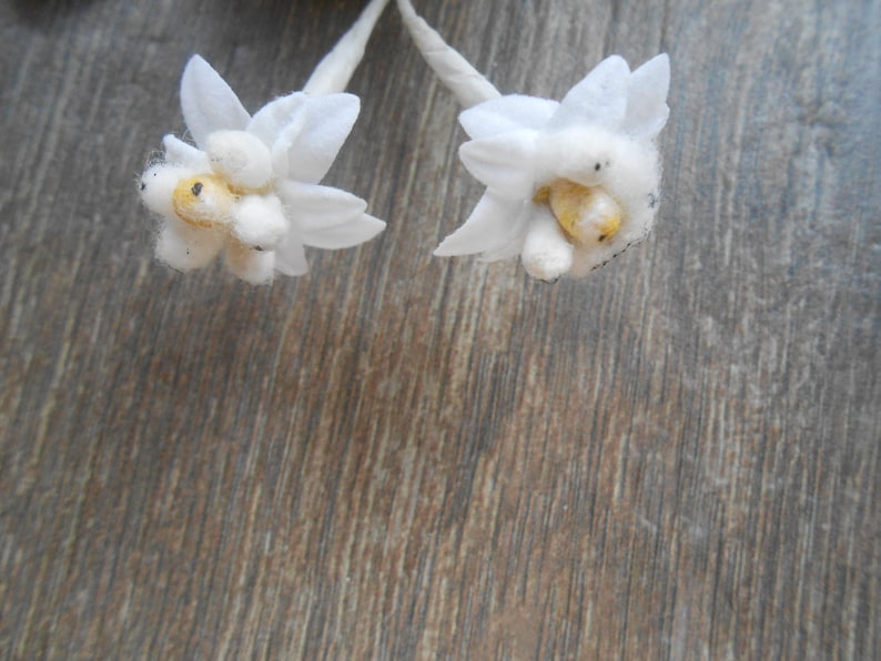 May include: Two white fabric flowers with yellow centres on a brown wooden background.