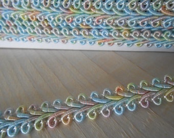 May include: Pastel-colored decorative trim with a looped design. The trim features a repeating pattern of swirls in shades of blue, pink, yellow, and green. The trim is stacked on top of each other, and is on a light-colored wooden surface.