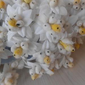 May include: A bunch of white felt flowers with yellow centres and black accents. The flowers are arranged in a bouquet and have a soft, fluffy texture.
