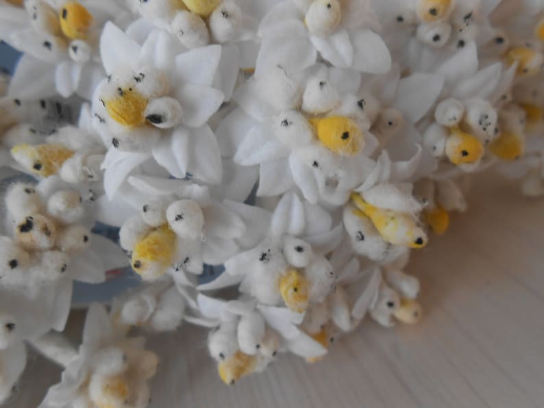 May include: A bunch of white felt flowers with yellow centres and black accents. The flowers are arranged in a bouquet and have a soft, fluffy texture.