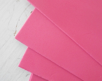 May include: Four sheets of vibrant pink foam are stacked, showing their edges. The foam has a slightly textured surface and a solid colour. The sheets are arranged on a white, textured surface.