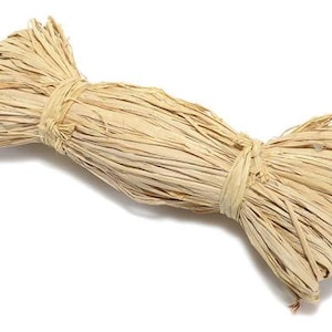 Può includere: Un fascio di fibra di rafia naturale, un tipo di spago naturale, di colore beige chiaro. La rafia è legata al centro, creando una forma a fiocco.