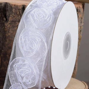 Può includere: Nastro bianco in organza con un motivo floreale. Il nastro è arrotolato su un rotolo bianco.